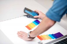 Messen der Farbe auf dem Papierdruck mit einem Spektrometer-Werkzeug am Schreibtisch der Druckerei